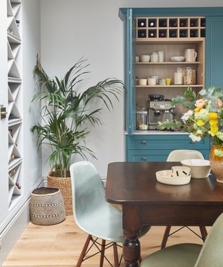 Blue painted kitchen storage with chunky wooden dining table and indoor plant