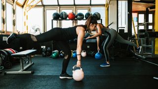 Two women performing the single-leg Romanian deadlift with kettlebells in the gym