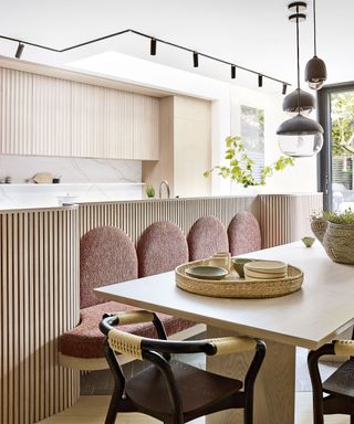 Modern kitchen with wooden fluting on kitchen island, seating area around wooden dining table, track and pendant lighting
