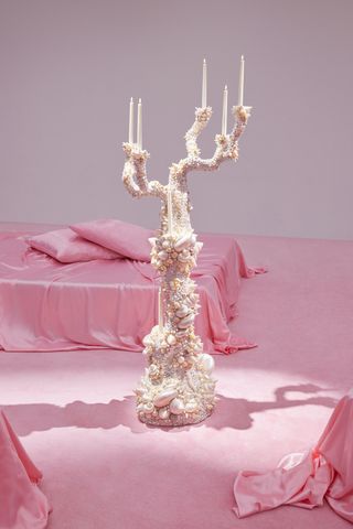 A candelabra by Sylvie Macmillan for Acne Studios S/S 2023 show set between platforms with pink sheets and pillows on them.