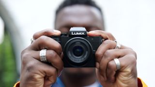 Panasonic Lumix G100 camera held in two hands in front of a mans face