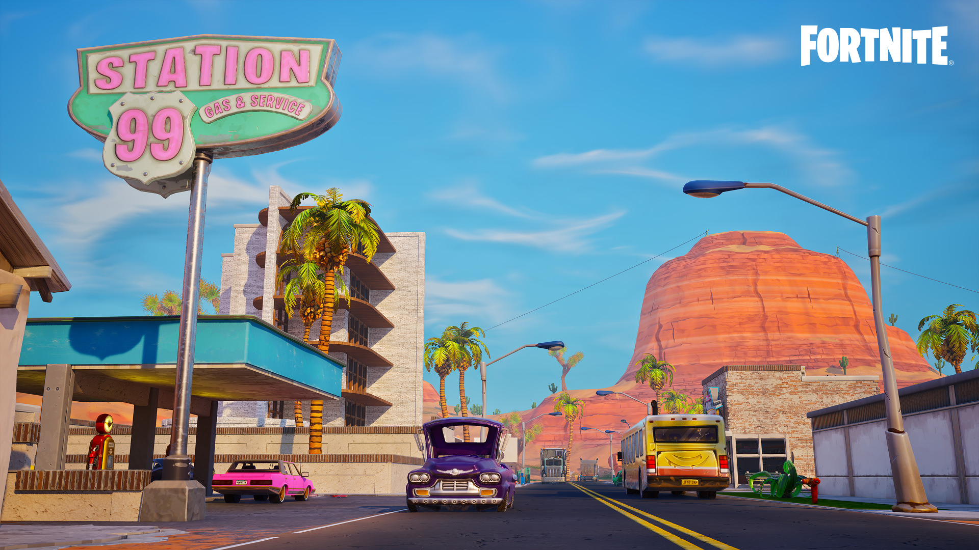 A town in Fortnite, with a gas station, a 'Station 99' sign, several cars, a tall apartment building and some palm trees, with an orange sun-baked mountain in the background.