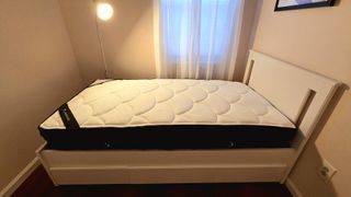 DreamCloud Hybrid Mattress right after being removed from boxing and plastic wrap on our tester's white Ikea platform bed base with headboard, next to a window with sheet curtains