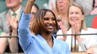 Denise Lewis smiling and waving to the crowd, with an ombré brunette bob and wearing a blue blazer