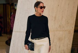 Woman in black crewneck sweater and white skirt.