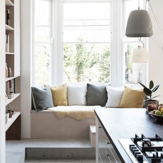 bay window seat with yellow grey and white cushions beside bookcase in open plan kitchen