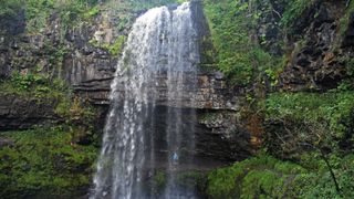 Man wearing Montane Cetus Lite Waterproof Jacket while hiking in under the Henrhyd Falls waterfall