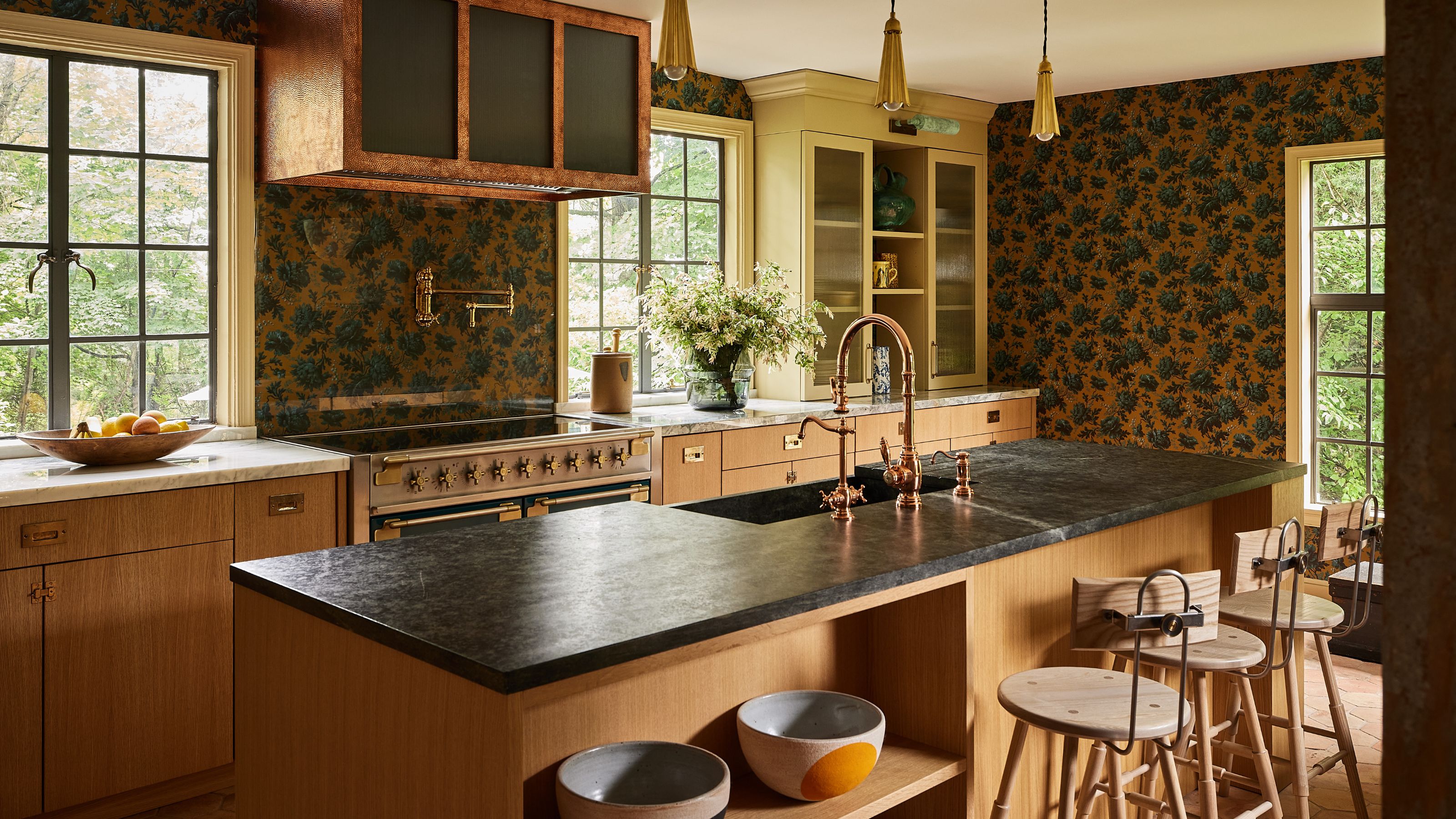 a cozy warm mustard and wood kitchen with wallpapered walls, a large kitchen island with a farmhouse wooden table