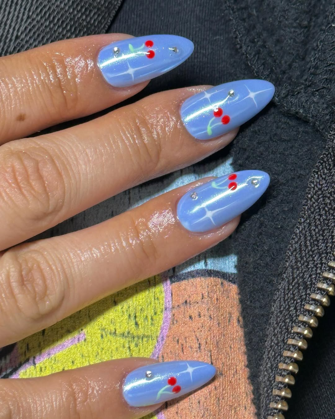 a person wearing blue chrome nails with a cherry design