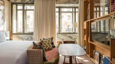 A hotel room with stone accents, a large bed, a tv unit and window treatments