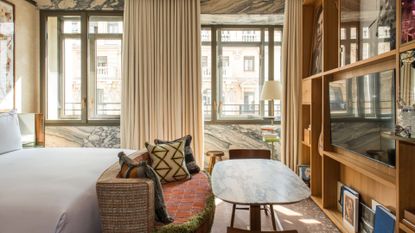 A hotel room with stone accents, a large bed, a tv unit and window treatments