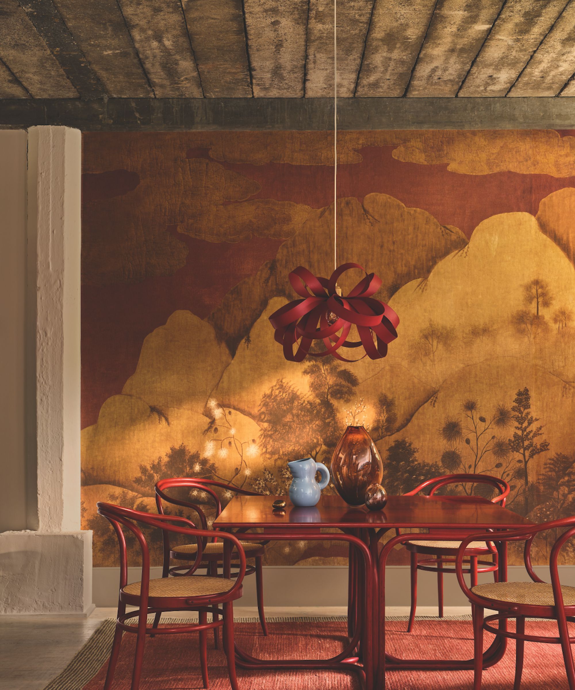 Rustic modern dining room with a red and gold wall mural and red dining table and chairs with a wooden Tom Raffeild light fixture