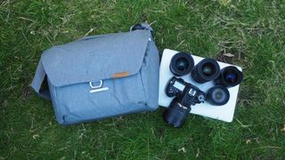 Peak Design Everyday Messenger, pictured on grass next to a camera and four lenses