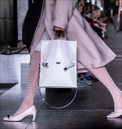 A model walks at Tory Burch with a white buckled tote bag