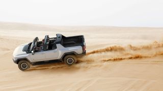 A white Hummer EV driving on a sand dune