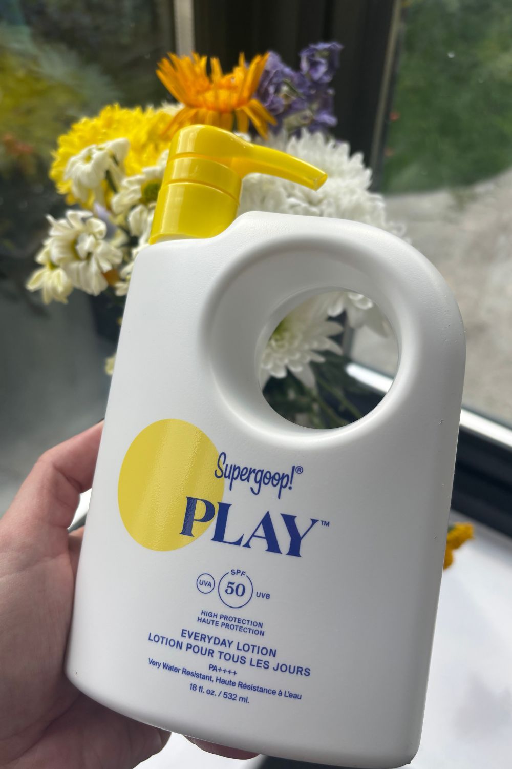 a hand holding a jumbo bottle of supergoop! play spf