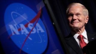 a man in a suit smiles at a podium in front of a nasa logo