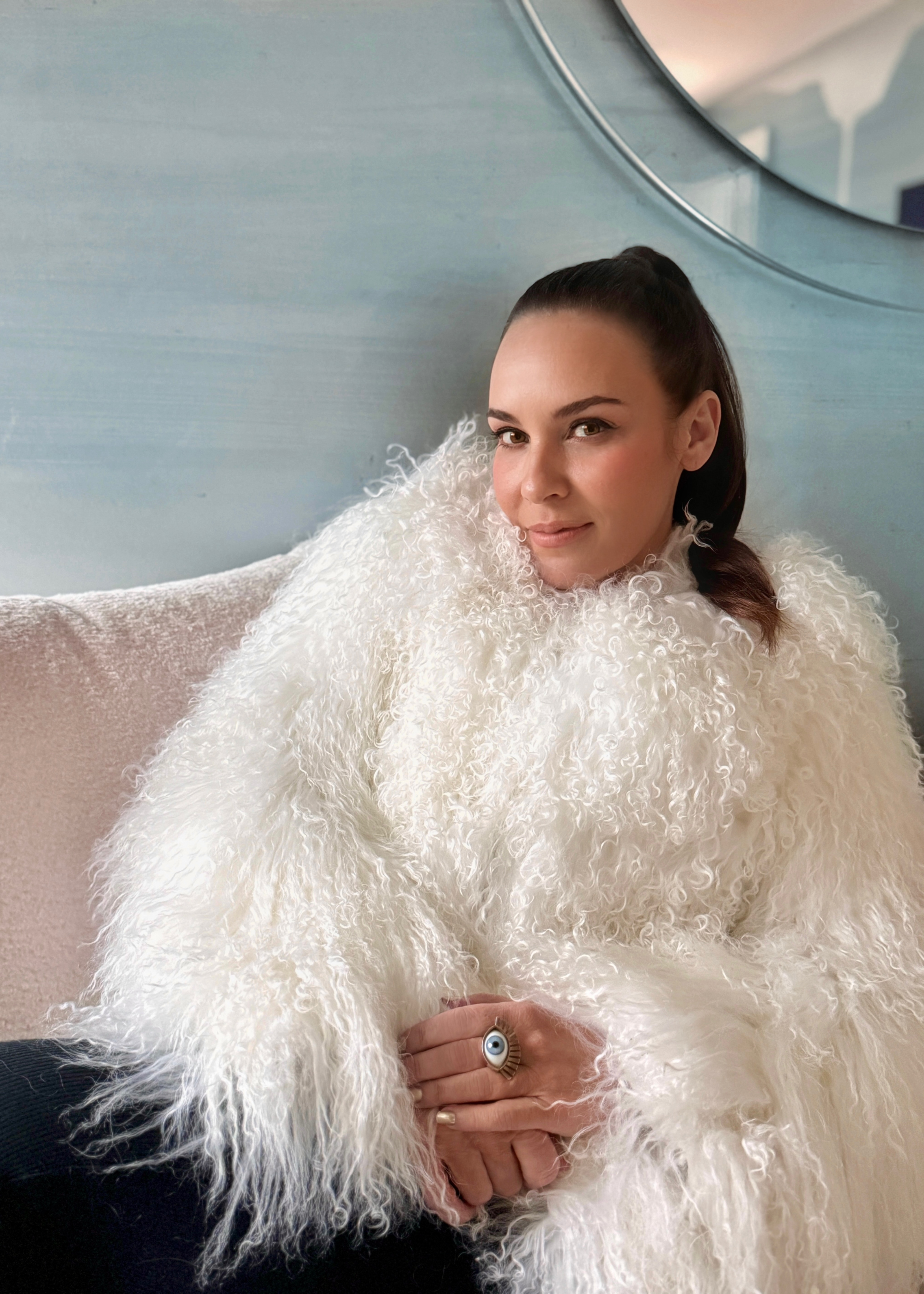 cara woodhouse headshot: a woman with dark brown hair tied back slightly smiling at the camera wearing a white fluffy jacket and black trousers