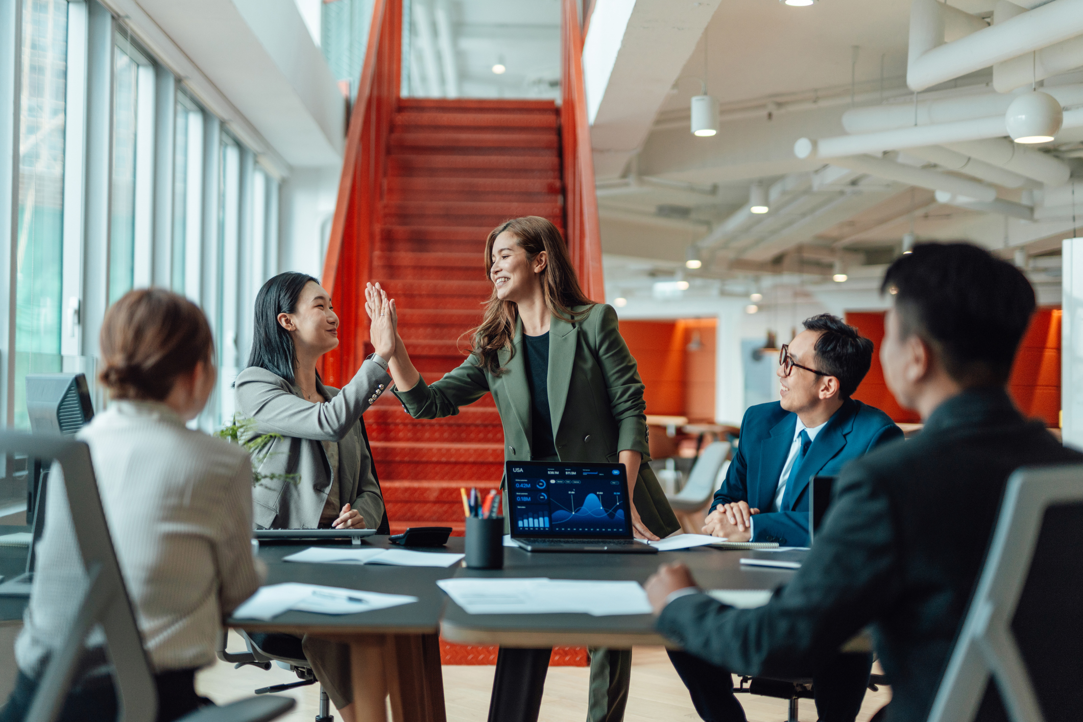 Employees around a table in an office with two employees high fiving