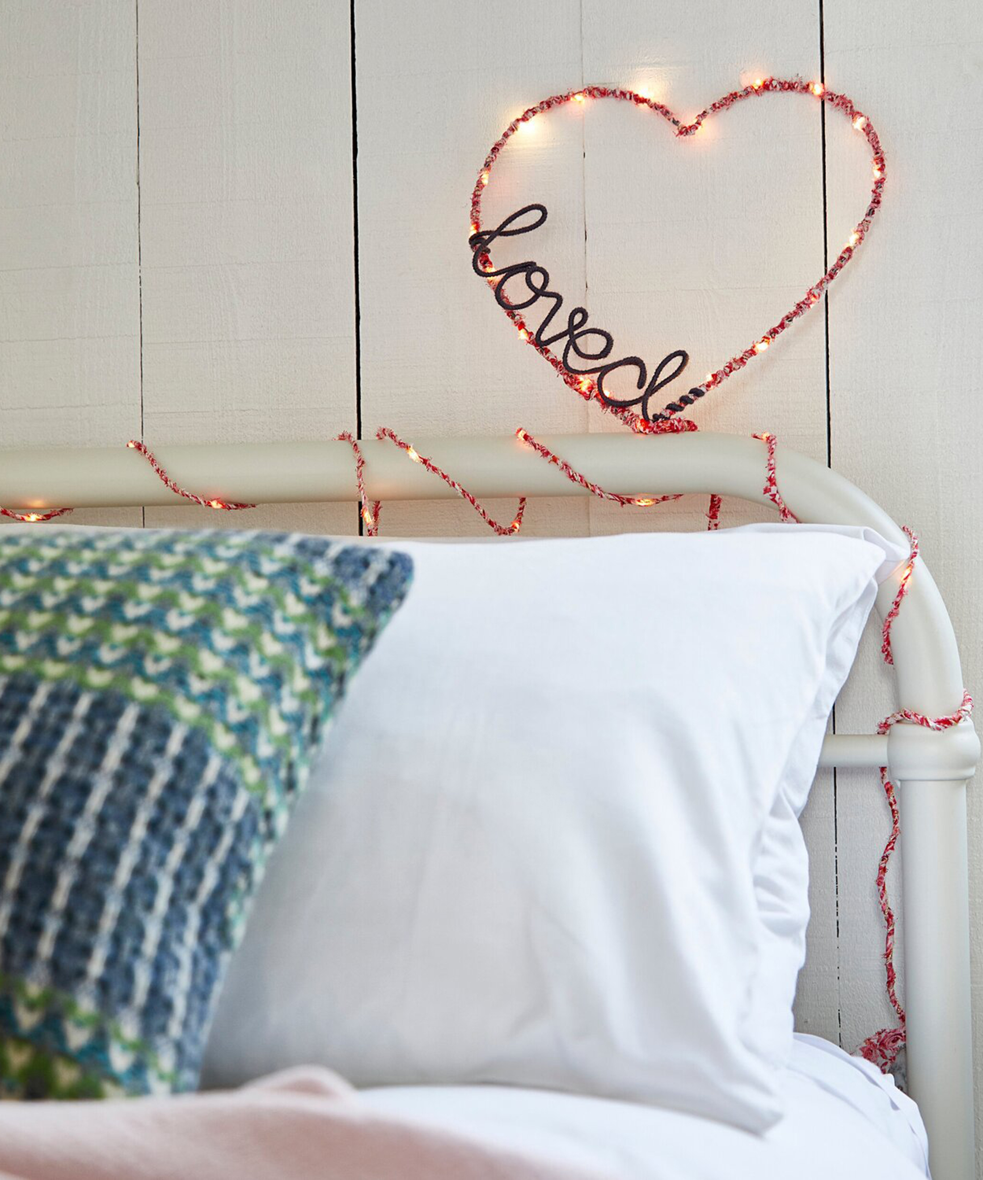 A bed with handmade heart decoration wrapped in textile fabric and fairy lights