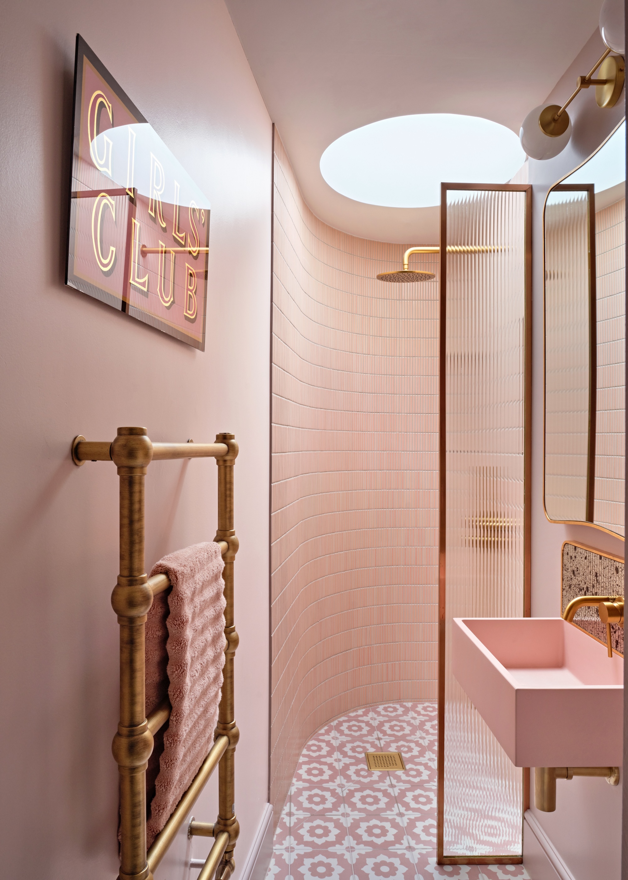 A blush pink bathroom with gold features in different parts of the space. There is a towel rack with a pink towel and a pink sink.