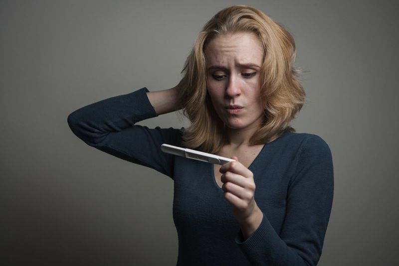 A woman looks confused at a pregnancy test.