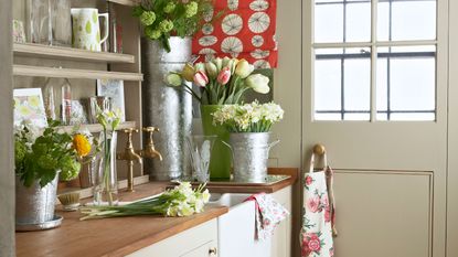 Narrow utility room ideas showing built in shelving behind a sink and decorative fresh flowers
