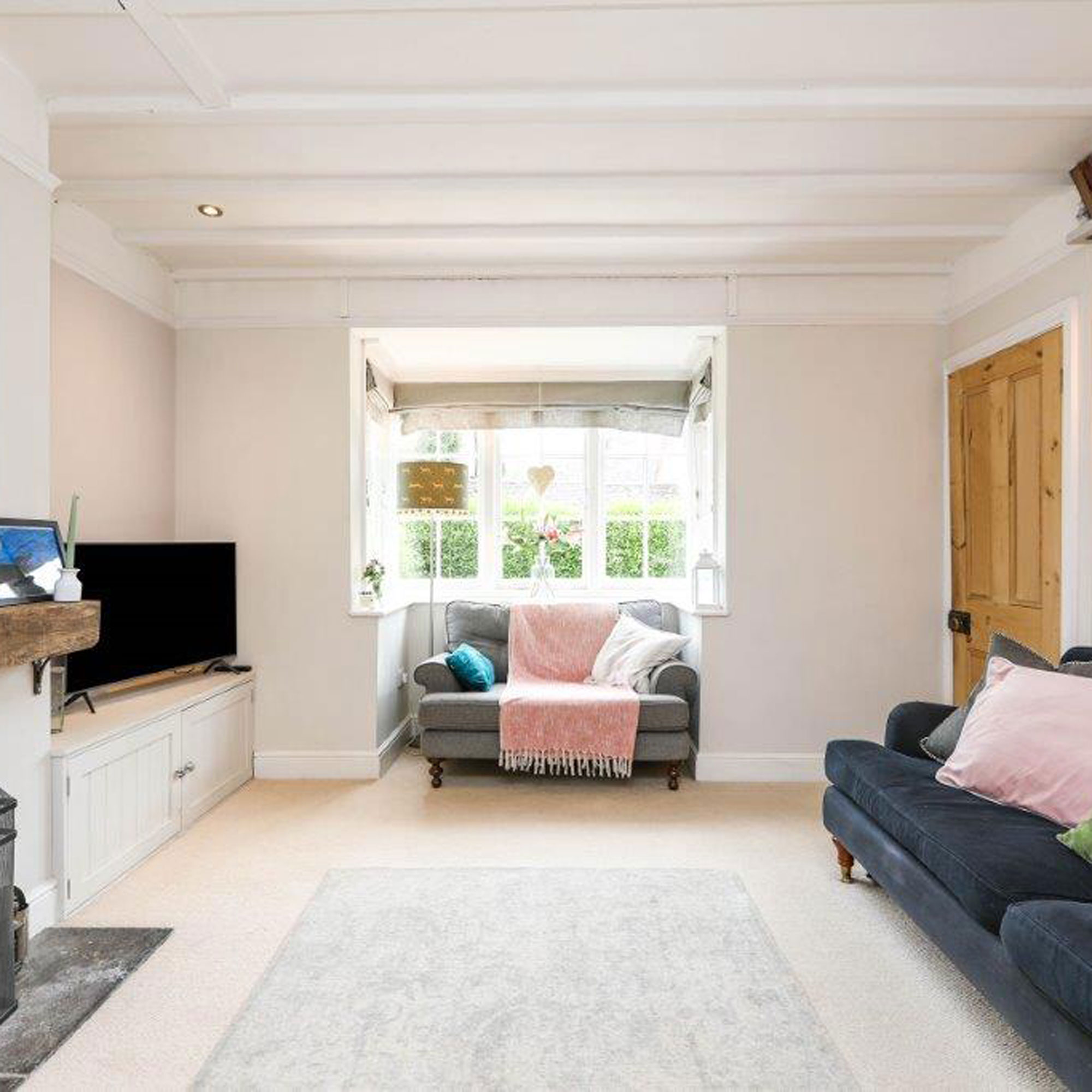 pink living room with navy sofa and bay window with pine door