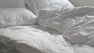 an unmade bed with duvets and pillows and white bed covers