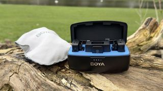 Boyamic microphone in its charging case on a tree stump