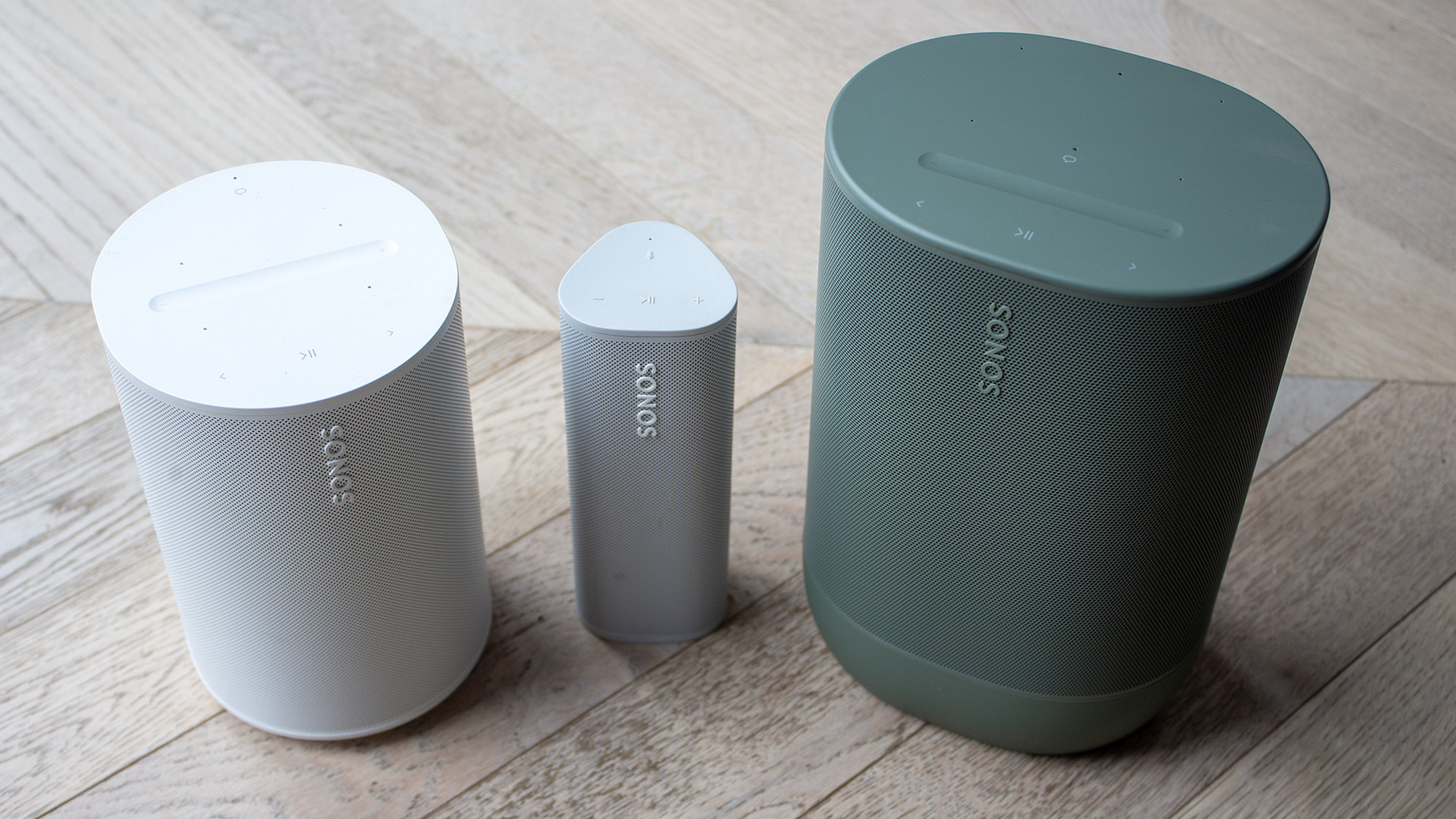 A side-by-side view of a white Sonos Era 100, a grey Roam 2 and a green Move 2.