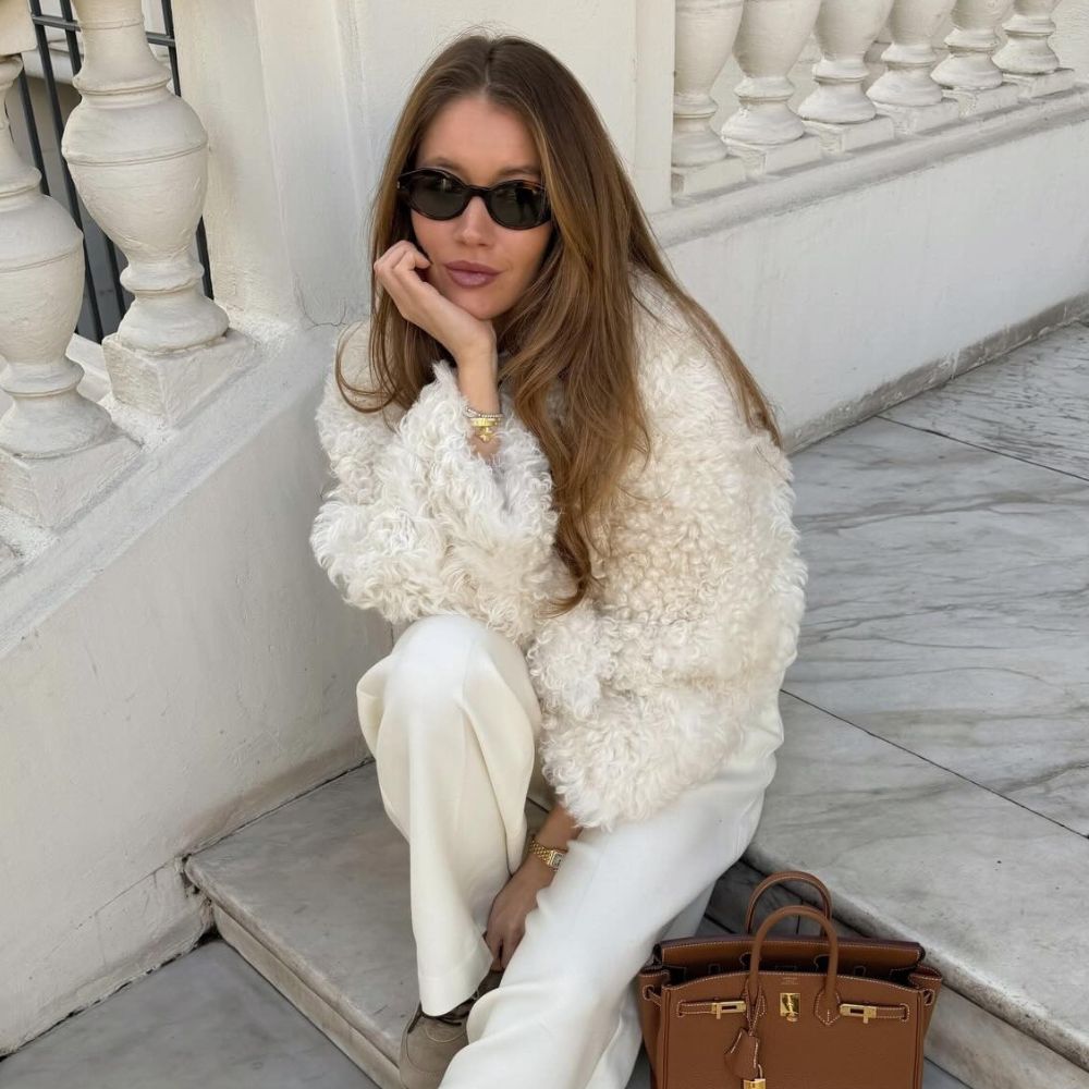 Influencer @lovisabarkman sits on steps outside wearing a cream fur jacket with cream trousers and shearling trainers.