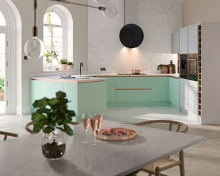 A kitchen with mint green cabinets, smart wall and pendant lighting, and a dining table with wooden chairs