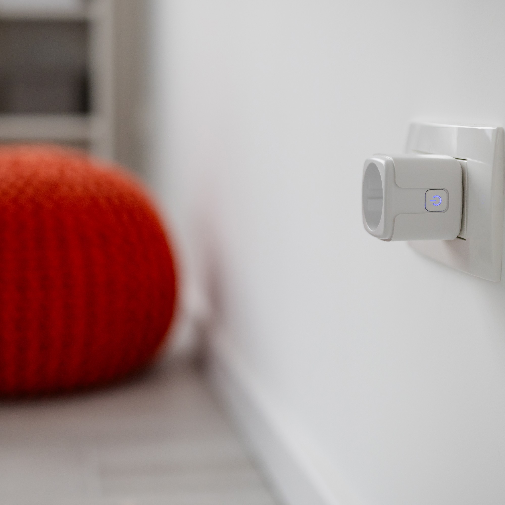Smart plug in wall socket, with a burnt orange knitted pouffe and a plant in the background