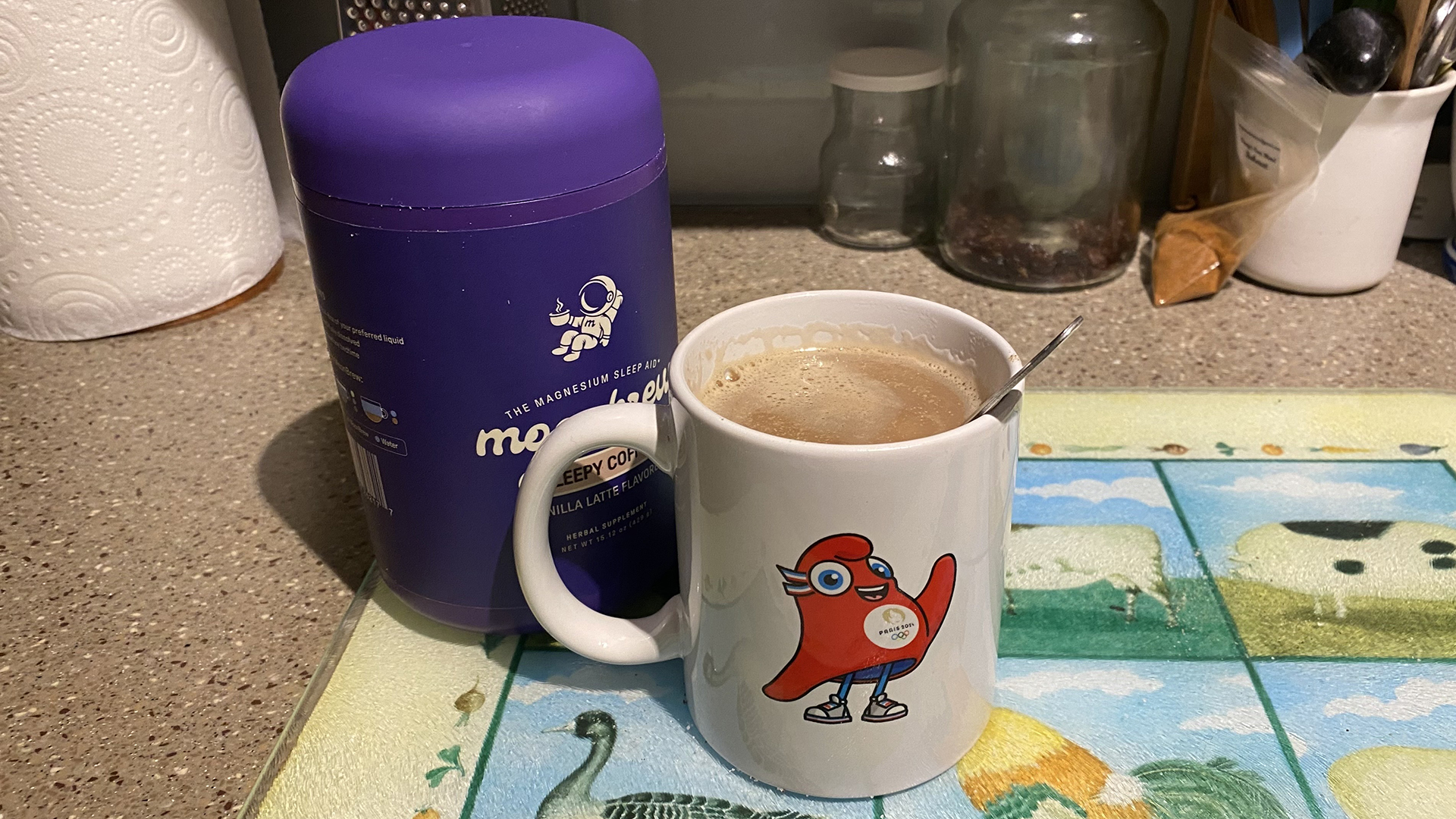 A tub of Moonbrew Magnesium Vanilla Latte and a mug, filled with Moonbrew Vanilla Latte, on a (slightly messy) kitchen counter