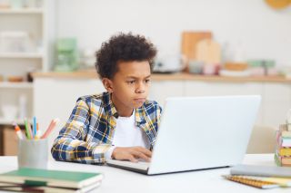 Middle school boy works at laptop computer
