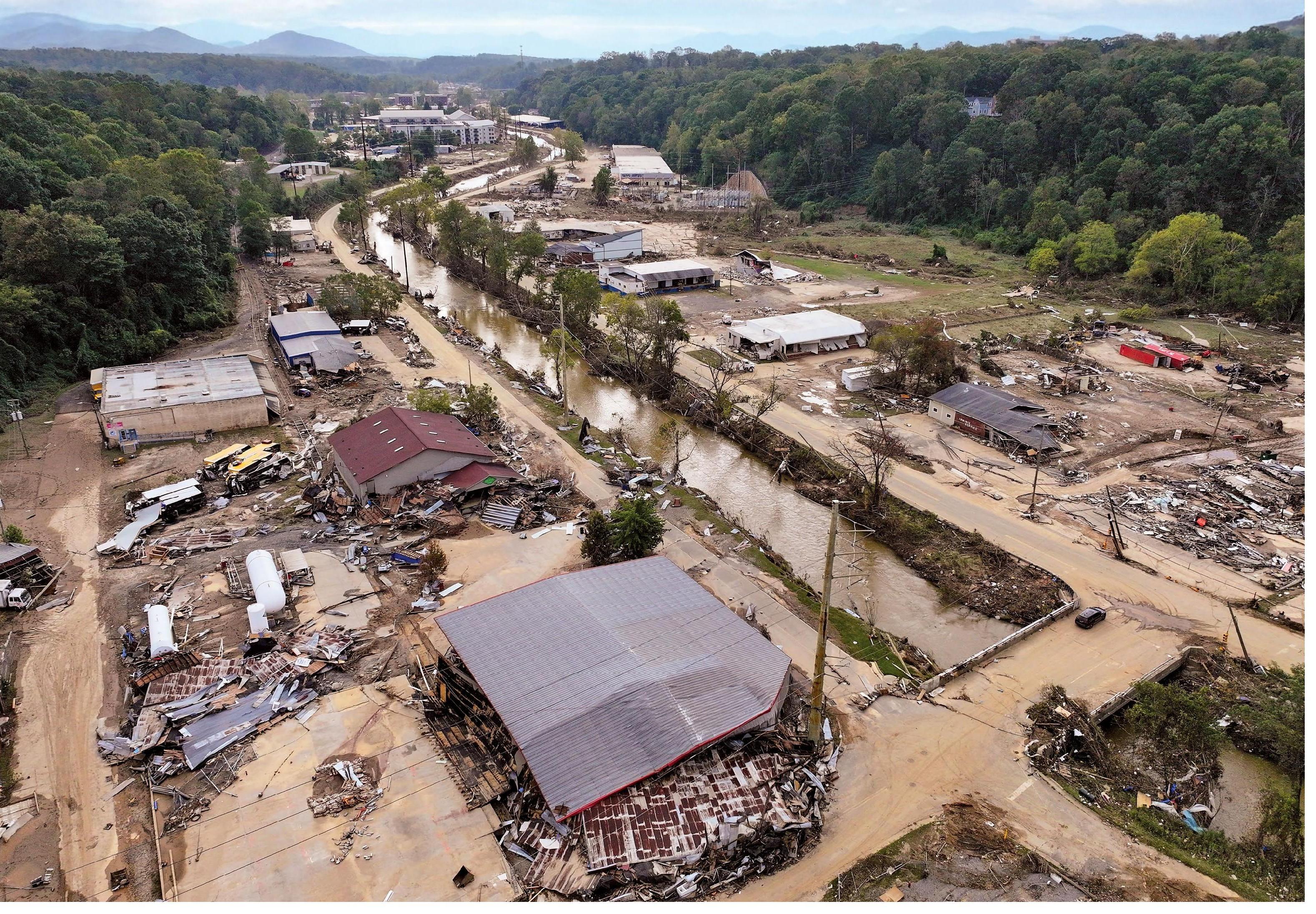 Aerial view of extensive damage and flooding in Asheville, N.C., following Hurricane Helene, showcasing destroyed buildings and debris along a flooded area.