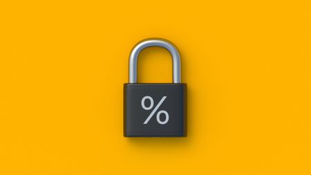 A padlock with a percent symbol on the front is against a bright orange background. This conveys the concept of fixed annuities, locking in an interest rate, or a fixed interest rate.