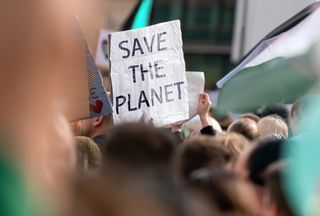 person holding "save the planet" sign in large crowd