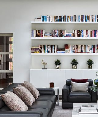 bookshelves in white living room with black leather armchair and couch