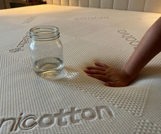 A jar of water and a hand resting on the surface of the Saatva Contour5 Mattress.