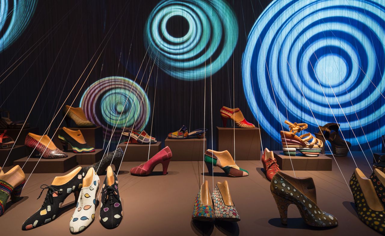 A display showcasing multiple heeled shoes on a brown surface with a siwrly blue backdrop