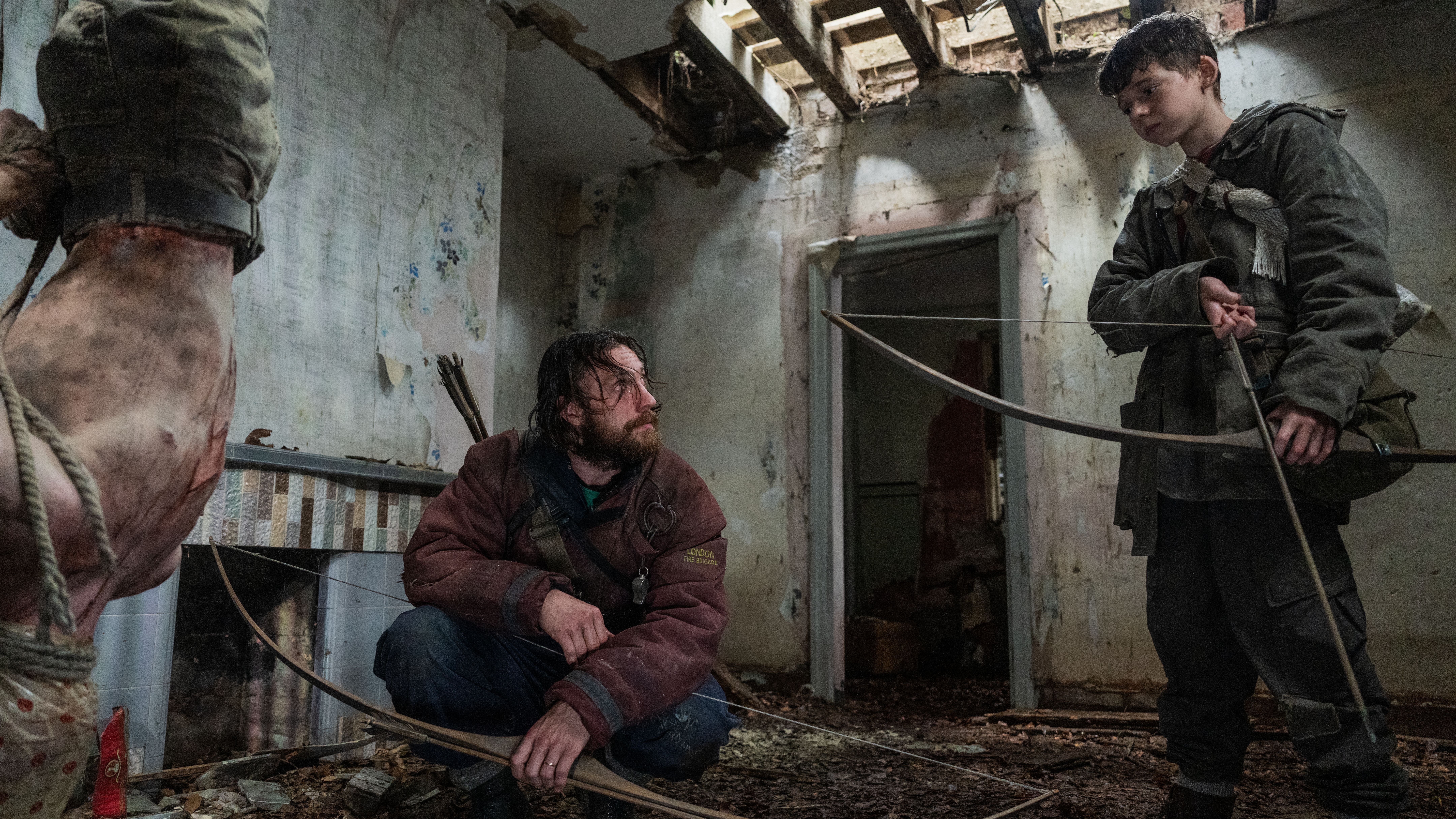 L-R: Jamie (Aaron Taylor-Johnson) and his son Spike (Alfie Williams) stand next to a hanging infected body in a scene from &quot;28 Years Later&quot;