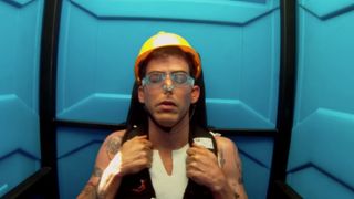Steve-O wearing a yellow hard hat with goggles on and a nose plug, with his eyes closed, prepared for the portapotty stunt.