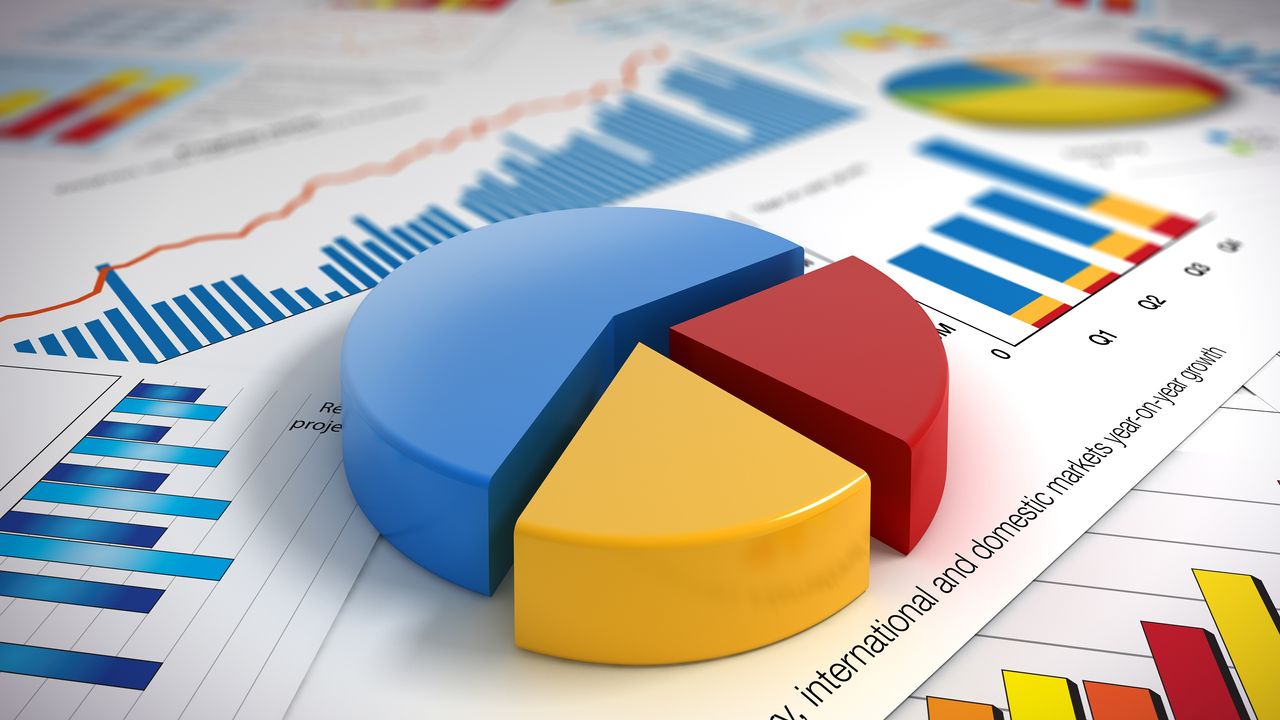 A pie chart made of blocks sits on top of paperwork with charts and graphs.