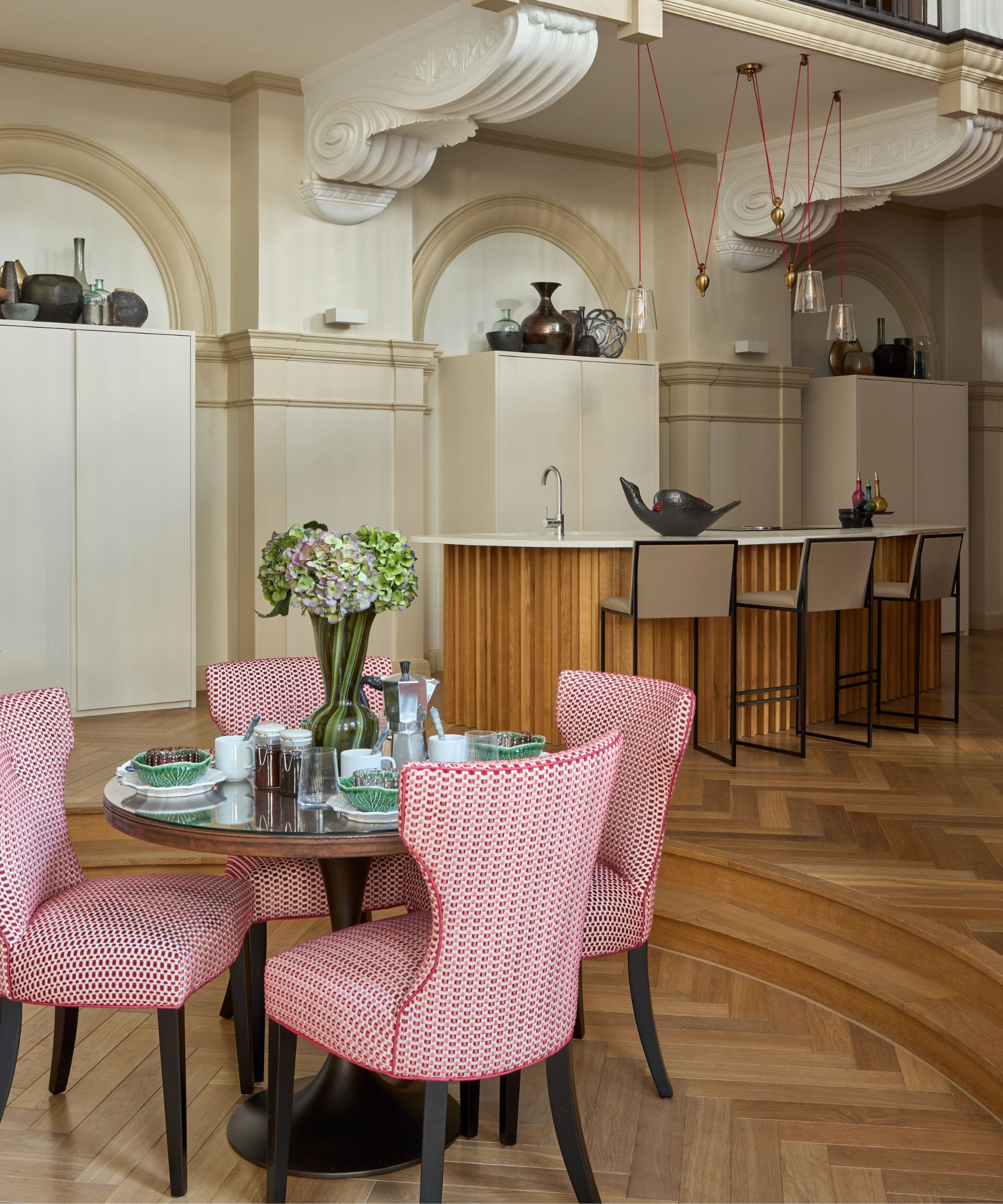 Open-plan dining and kitchen space with herringbone parquet wood flooring and patterned dining chairs.