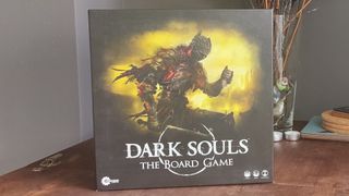 The Dark Souls board game box on a wooden table, with plants in the background