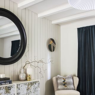Round black framed mirror on white panelled wall