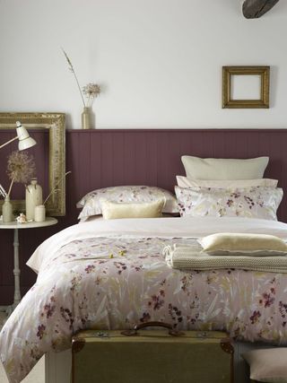 Bedroom with painted purple wall panels, patterned bed linen and decorative frames
