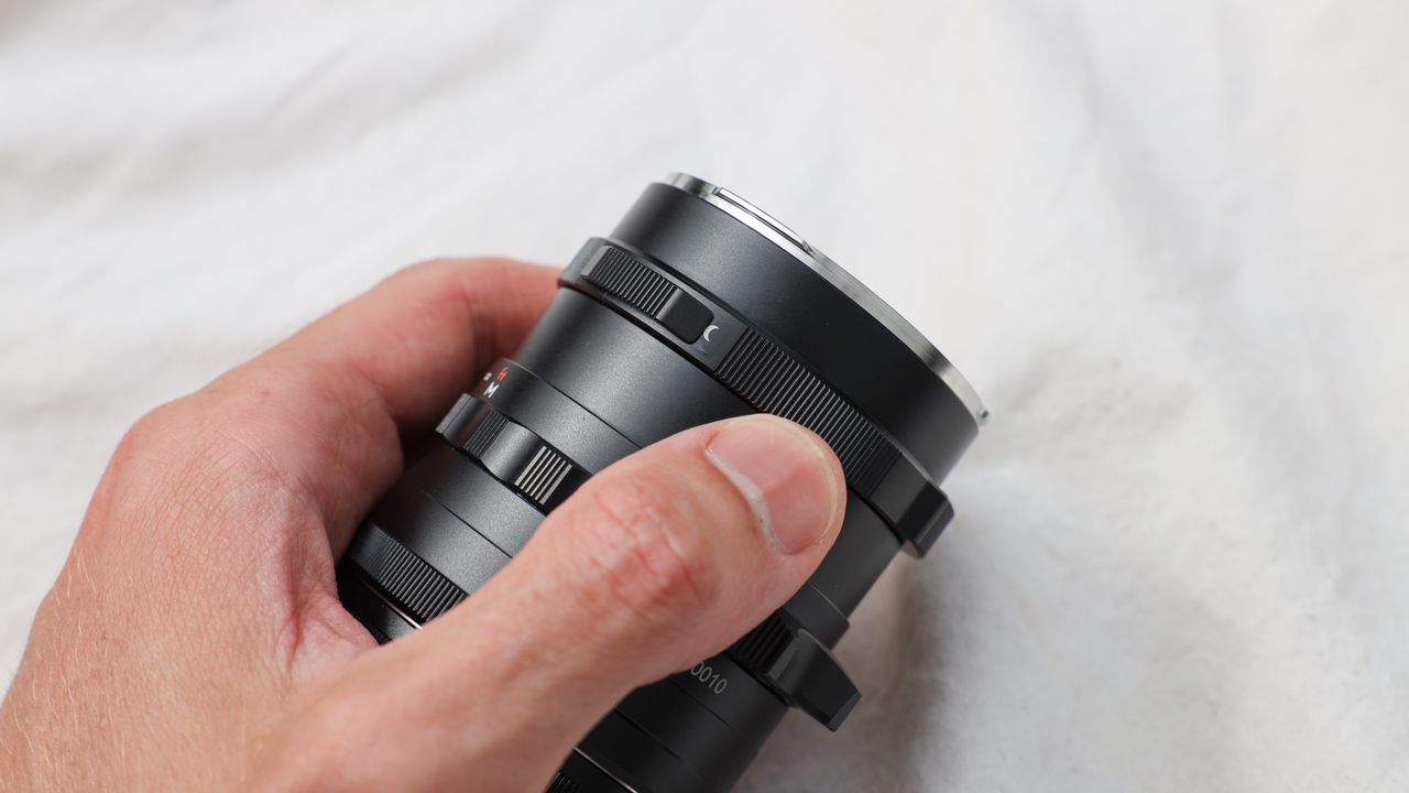Thypoch Simera 28mm f/1.4 lens held in a hand on a beige cloth